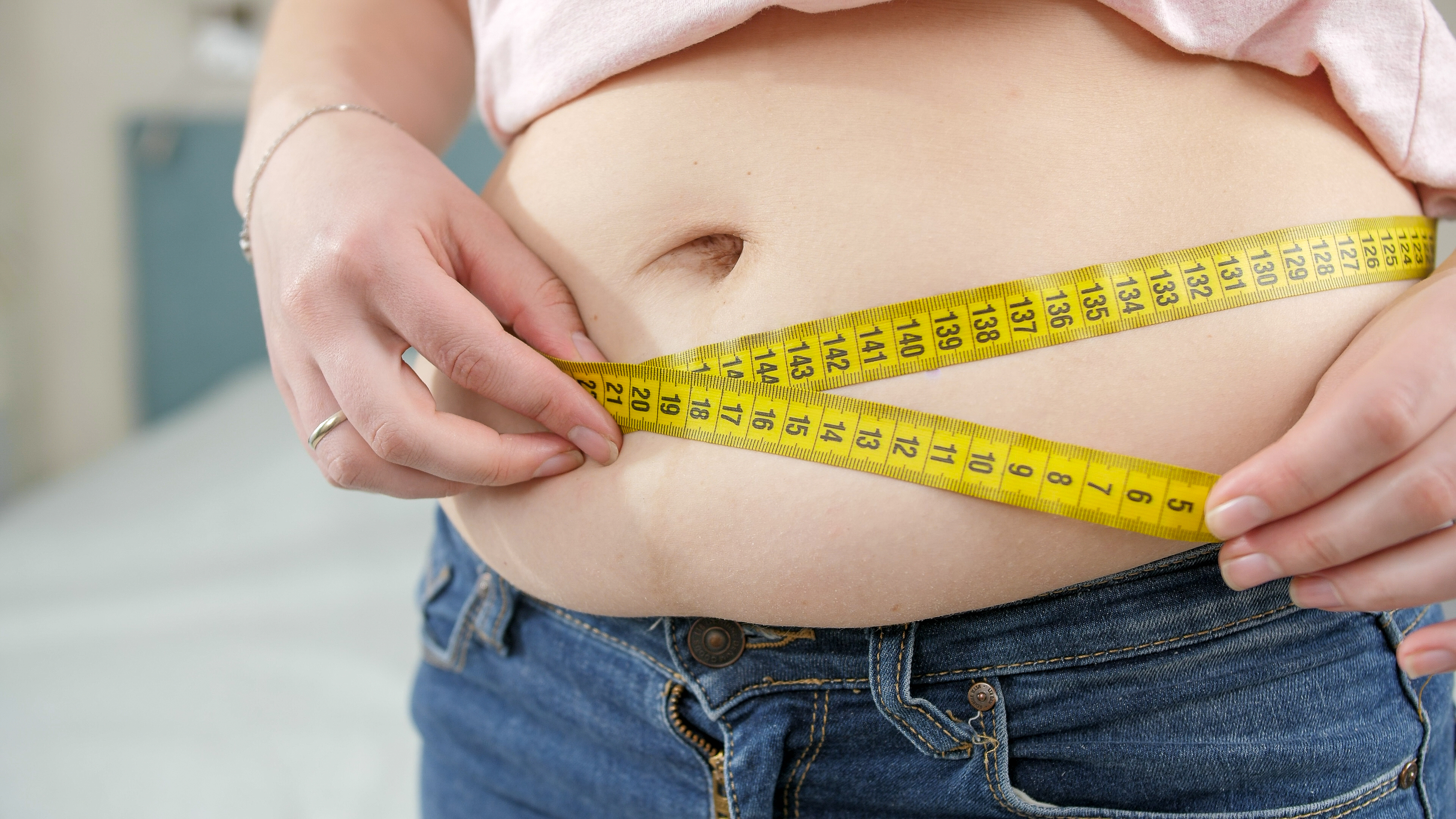 Closeup of young woman loosing weight measuring her waist. Concept of dieting, unhealthy lifestyle, overweight and obesity